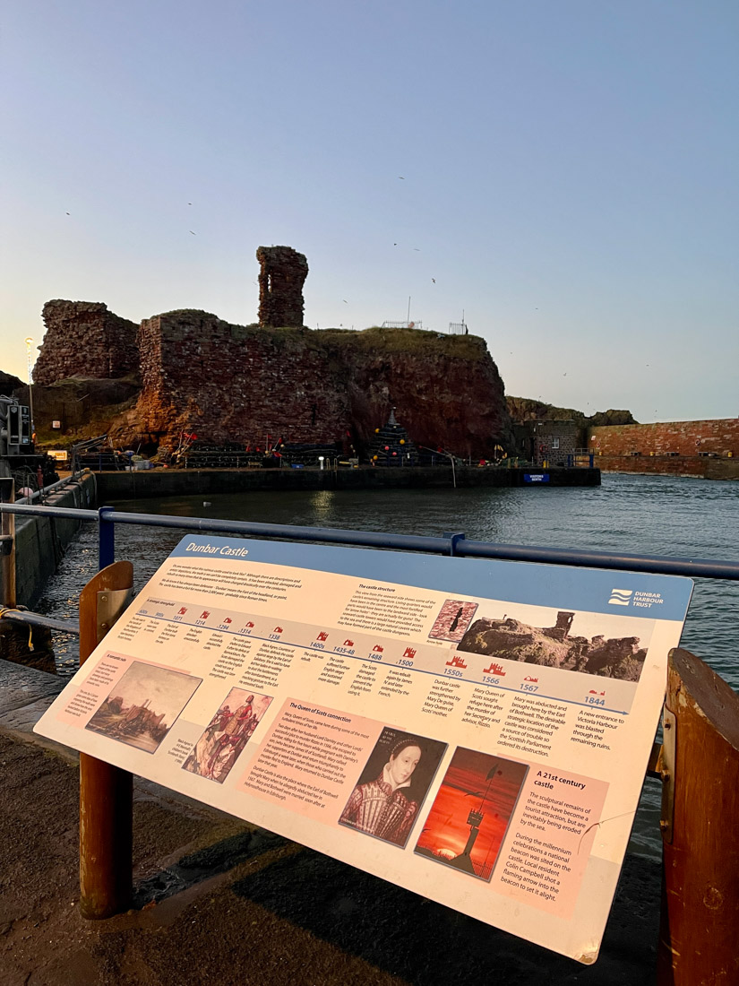 Dunbar Castle at night with sign explaining castle story