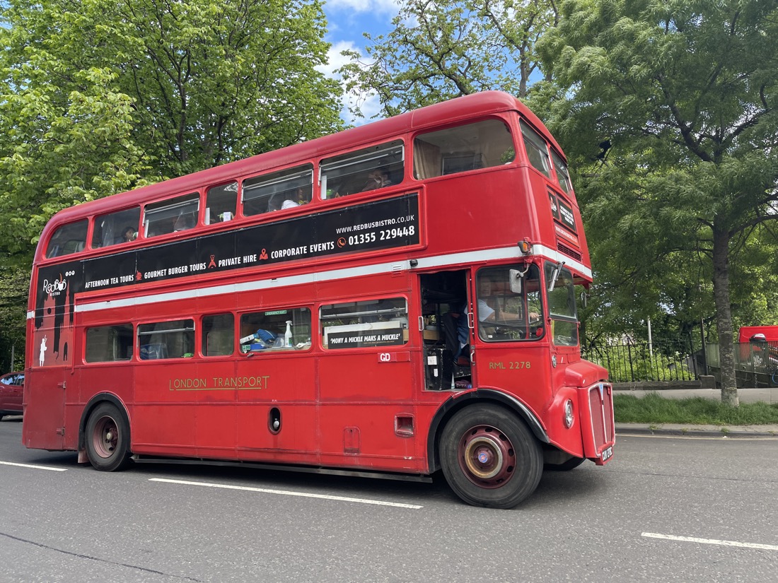 Vintage Red Bistro Bus Driving By Lush Greenery in Edinburgh