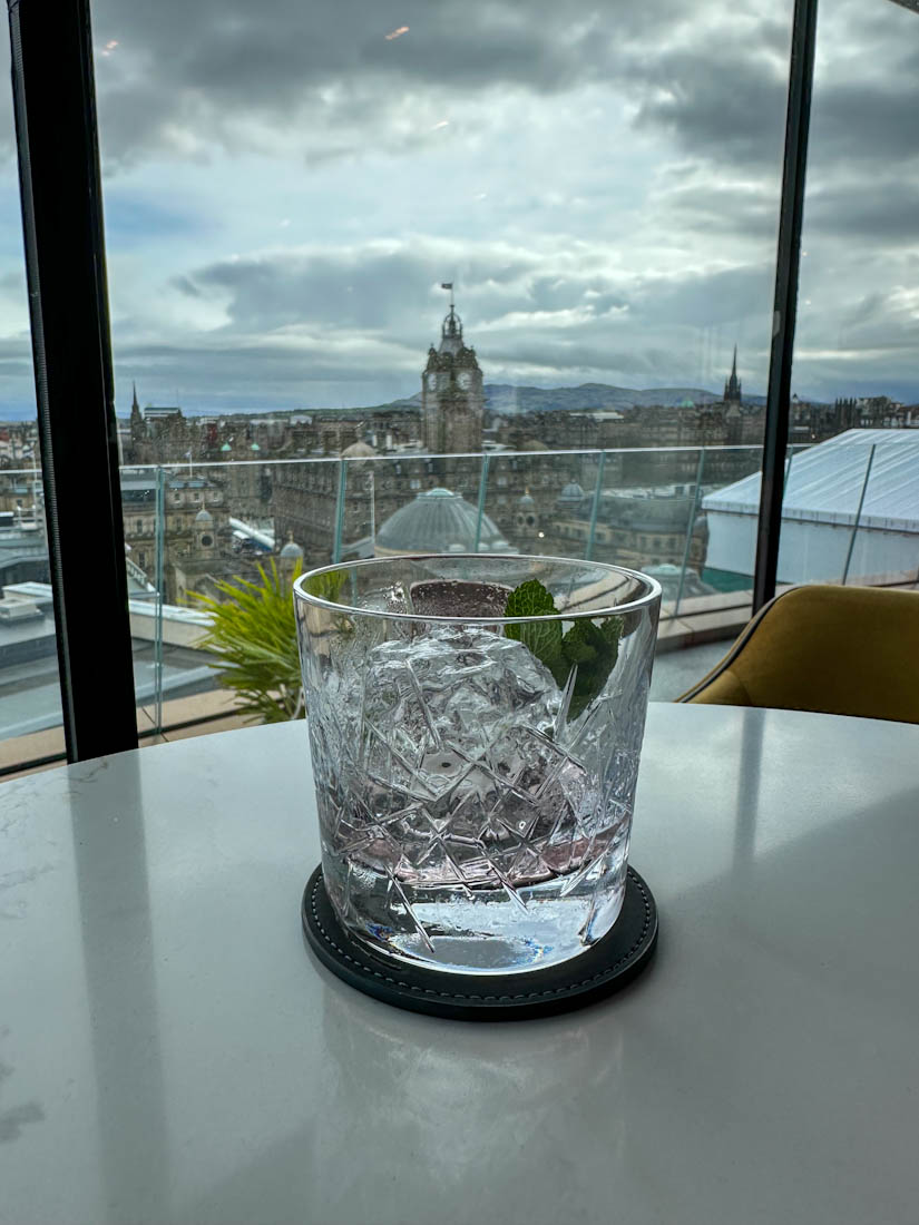 Cocktail on table in front of glass window at W Hotel Lounge with Edinburgh skyline 